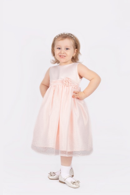 A little girl in a ball gown stands tall on a white background