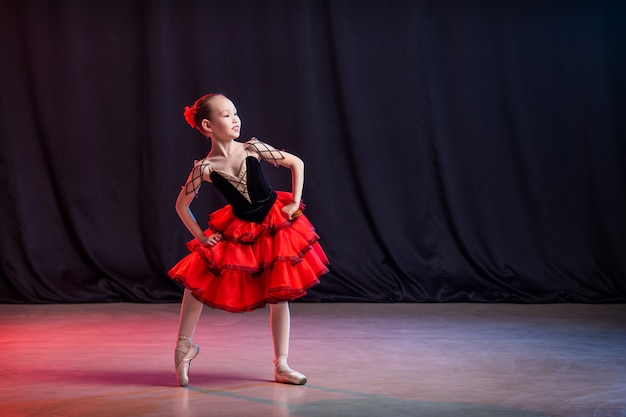 A little girl ballerina is dancing on stage in a tutu on pointe shoes with castanedas, the classic variation of Kitri.