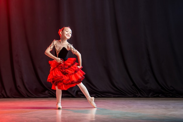 어린 소녀 발레리나가 Kitri의 고전적인 변형인 카스타네다가 달린 뽀인트 신발에 투투를 입고 무대에서 춤을 추고 있습니다.