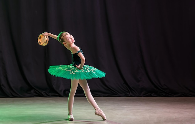 A little girl ballerina is dancing on stage in a tutu on pointe shoes with a tambourine, a classic variation of Esmeralda.