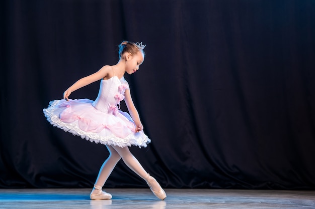 어린 소녀 발레리나가 포인트 슈즈 클래식 변형에 흰색 투투를 입고 무대에서 춤을 추고 있습니다.