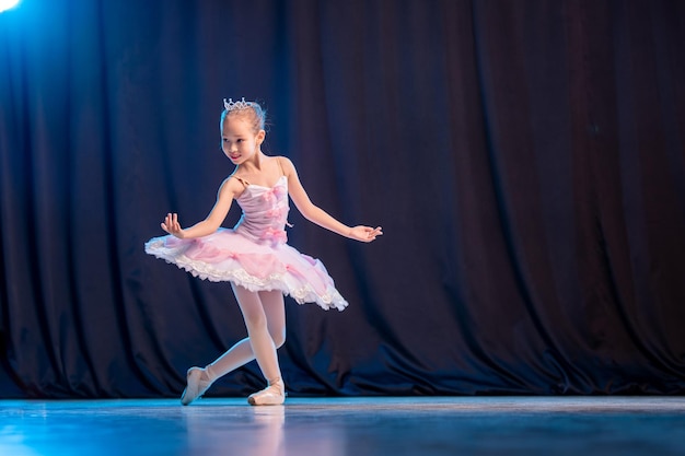 A little girl ballerina is dancing on stage in a white tutu on pointe shoes a classic variation.