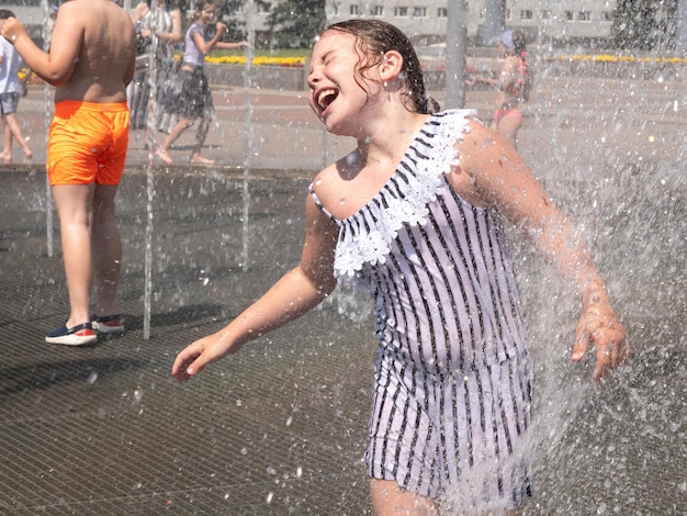 A little girl bathes in the heat in the spray of a fountain in the city square