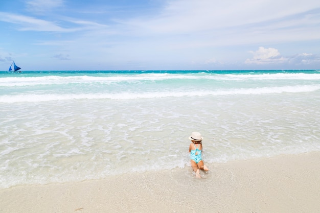 小さな女の子が白い砂のビーチで海を浴びる