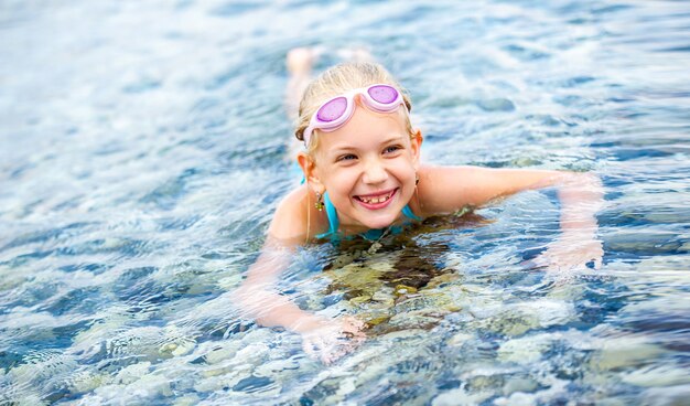 A little girl in a bathing suit lies in the sea and smiles.A little girl lies in the water and laugh