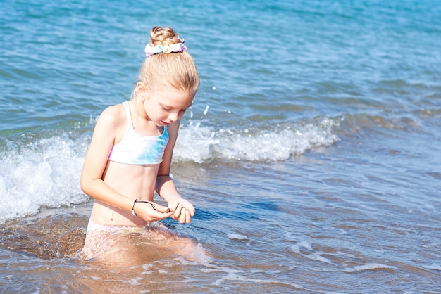 Маленькая девочка в купальнике, играя на пляже у моря