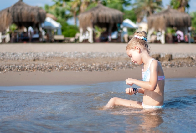 Маленькая девочка в купальнике, играя на пляже у моря