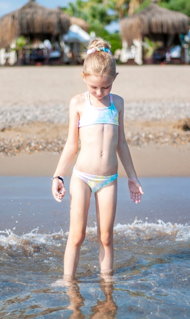 Little girl in a bathing suit playing on the beach by the sea