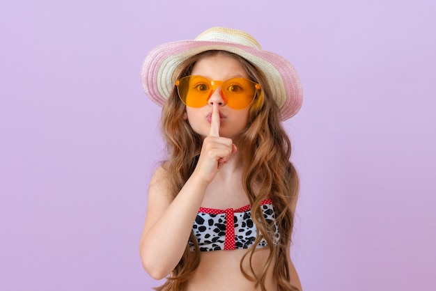 A little girl in a bathing suit shows a finger gesture please be quiet.