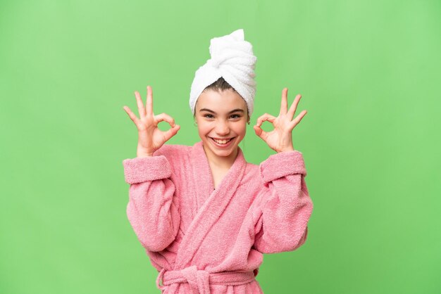 Little girl in a bathrobe over isolated chroma key background showing an ok sign with fingers