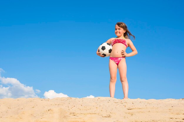 Little girl on the beach playing with a soccer ball. Sport games.