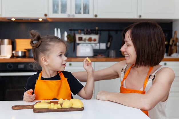 Little girl and beautiful mom are cooking vegetables at home kitchen