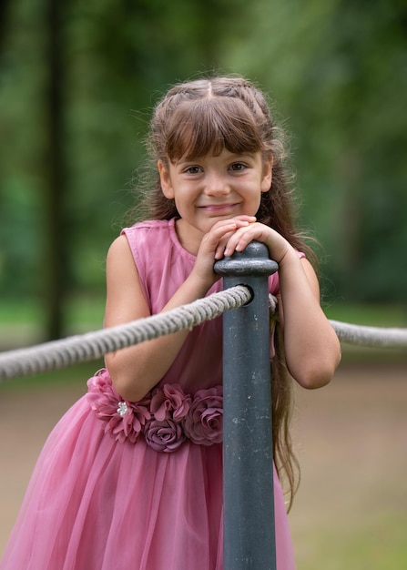 little girl in beautiful pink dress A child stands near a fence made of ropesLooks into the camera