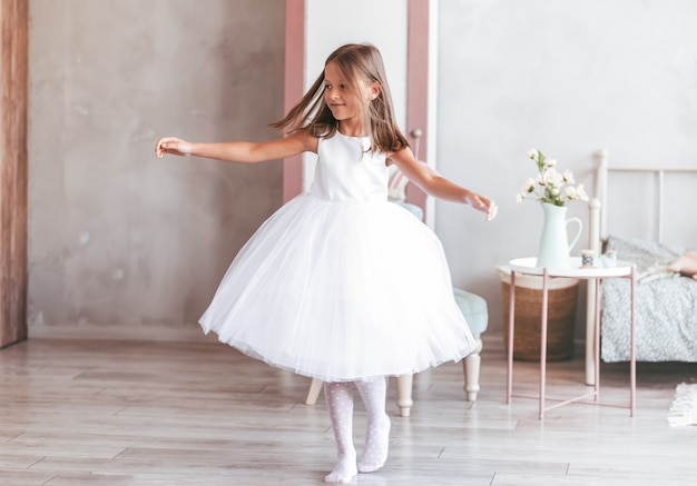 A little girl in a beautiful white dress dances in a light room. it's spinning to the music. happy childhood