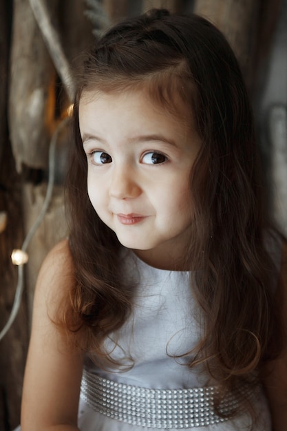 Photo little girl in beautiful white dress on a light wooden background. shine, silver, xmas