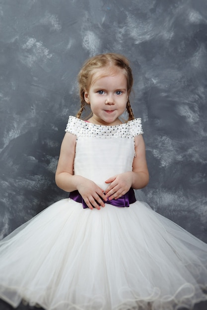 Little girl in beautiful white dress on a light wooden background