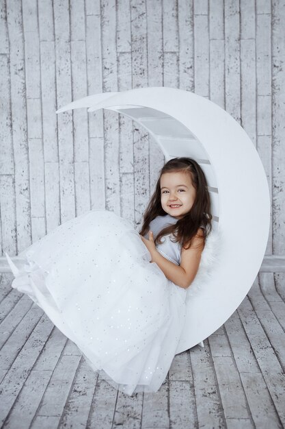 Little girl in beautiful white dress on a light wooden background