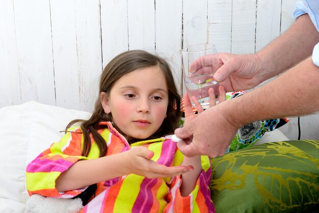 A little girl in bed taking tablet