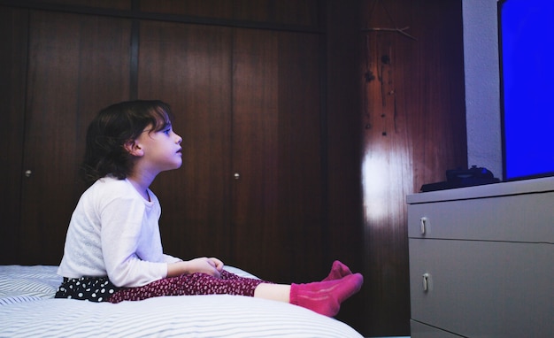 Photo little girl on bed watching tv