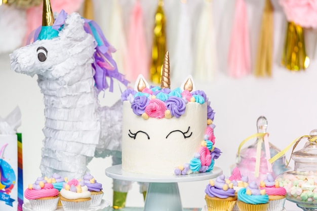 写真 ユニコーンケーキ、カップケーキ、sugaerクッキーと小さな女の子の誕生日パーティーのテーブル。