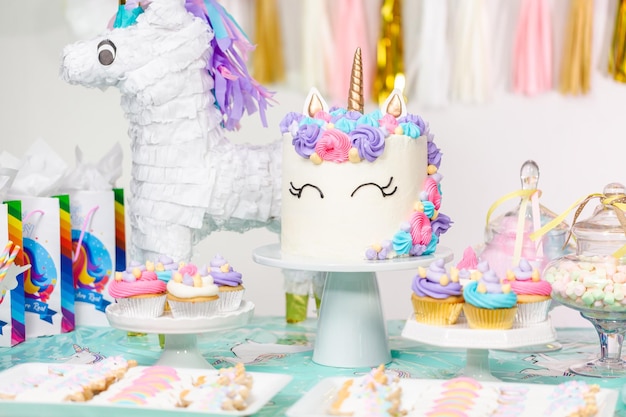 유니콘 케이크, 컵케이크, 슈가 쿠키가 있는 어린 소녀 생일 파티 테이블.