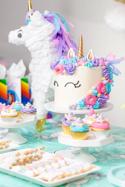 유니콘 케이크, 컵케이크, 슈가 쿠키가 있는 어린 소녀 생일 파티 테이블.
