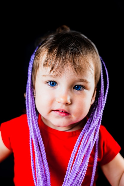 A little girl on a black background with Afro-pigtails, artificial plaited in elastic bands and put on cute