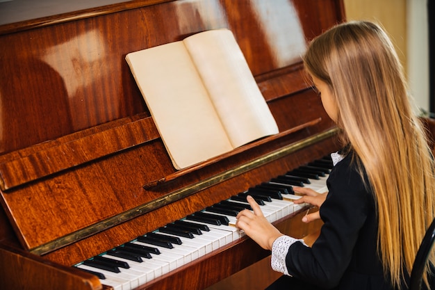 La bambina in un vestito nero impara a suonare il piano. il bambino suona uno strumento musicale.