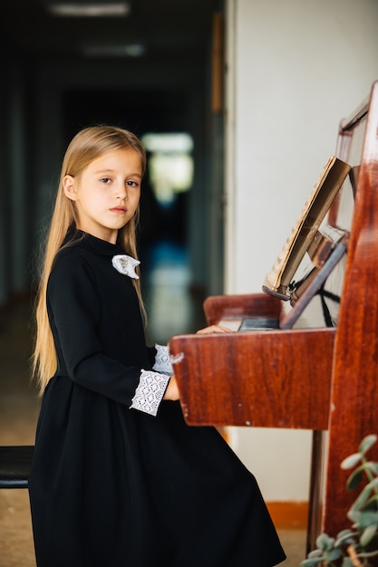 Маленькая девочка в черном платье учится играть на пианино. Ребенок играет на музыкальном инструменте.