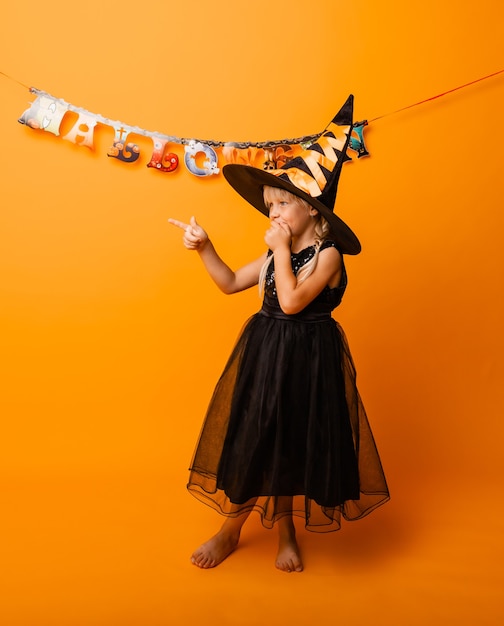 Little girl in black halloween costume laughing and looking at the camera, jumping and having fun, isolated on yellow background. halloween