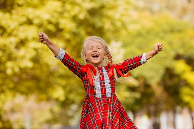 Abito plaid rosso bambina di prima elementare bionda sorridente nella strada