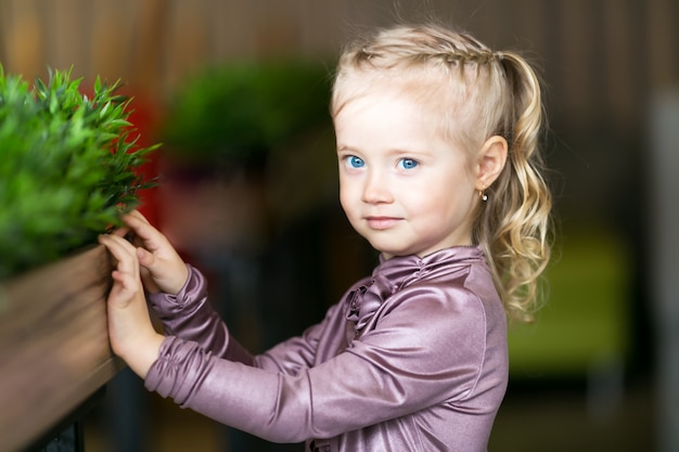 Little girl blonde with blue eyes in a flower bed with green grass