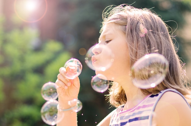 Маленькая девочка дует мыльные пузыри в парке