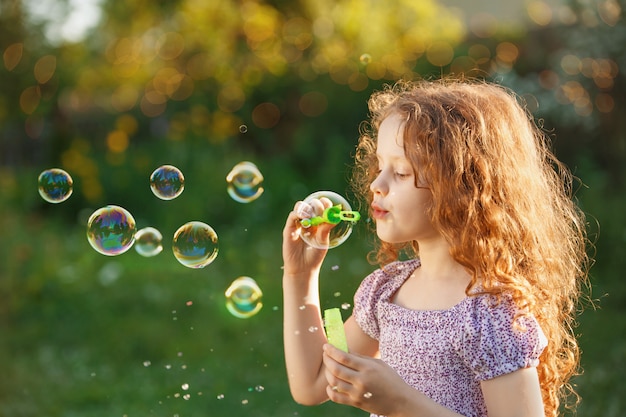 Photo little girl blowing soap bubbles in summer park.