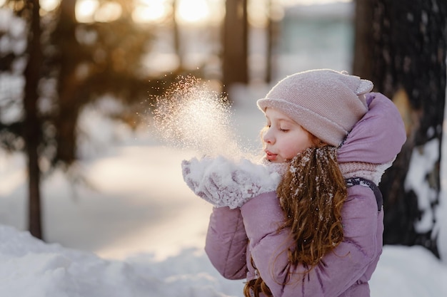 小さな女の子は、雪片のボケ味の背景にミトンで雪を吹く