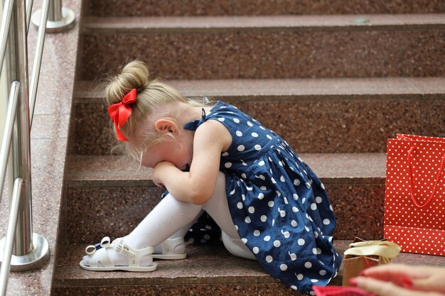 Little girl in a blue dress sits on the steps and cries