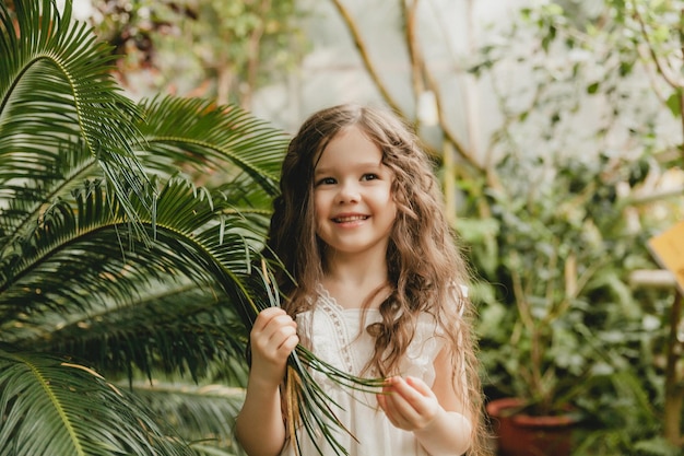 Bambina nel giardino botanico una ragazza in abito bianco ride vicino alle foglie di palma