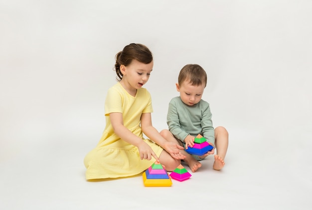 A little girl and a boy are playing with a colorful pyramid on a white background