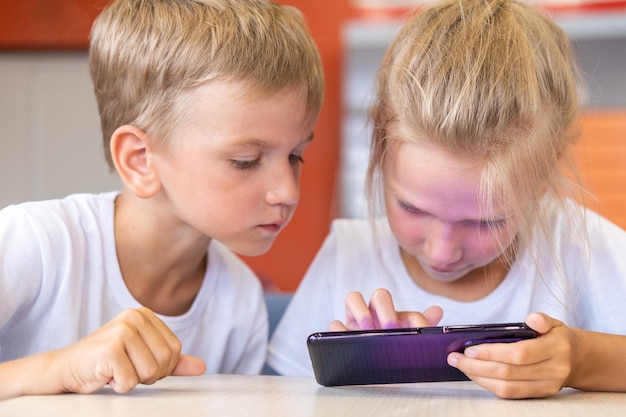 Una bambina e un ragazzo guardano cartoni animati sul telefono seduti a un tavolo i bambini giocano a un gioco online