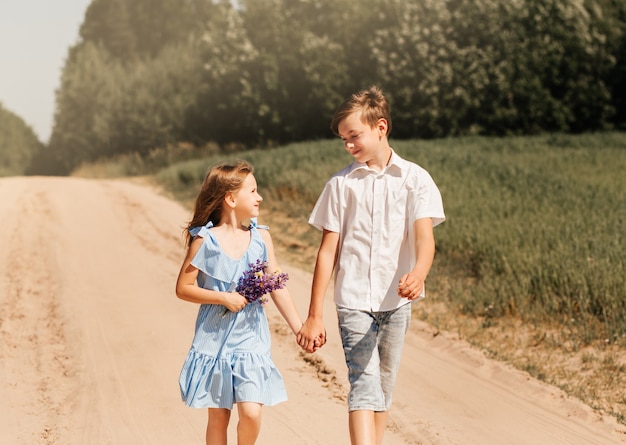 晴れた日に自然の中で手をつないでいる小さな女の子と男の子の兄と妹。国の子供たち。