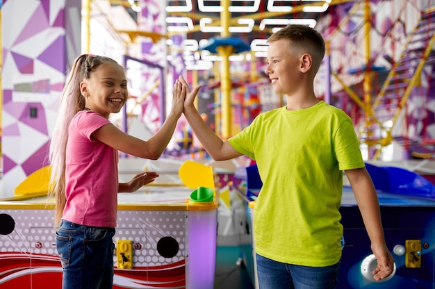 小さな女の子と男の子は、エンターテイメントセンターでエアホッケーをします。楽しんでいる子供たち、遊び場での子供たちのスポーツ競技、幸せな子供時代