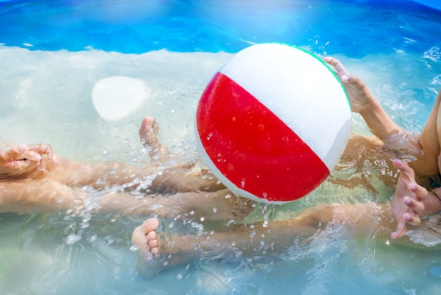 La bambina ed il ragazzo giocano con la palla sulla piscina all&#39;aperto.