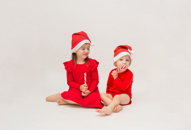 Little girl and boy in red caps with lollipops on a white wall with a copy of space