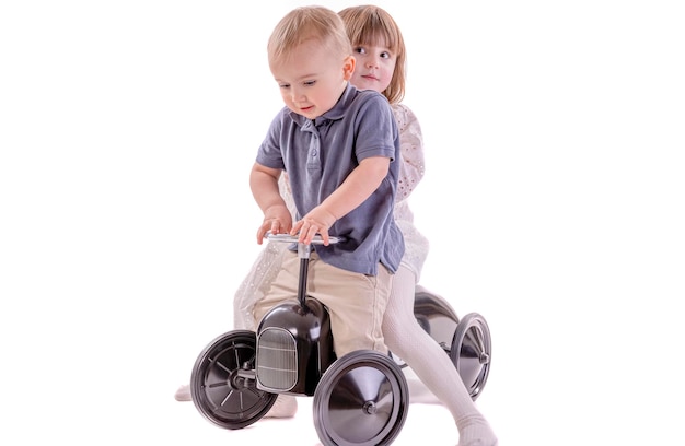 Little girl and boy riding Retro style toy car. Brother and sister riding old metal pedal car