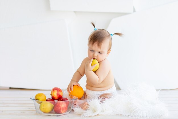 A little girl in a bright room sitting with a plate of fruit