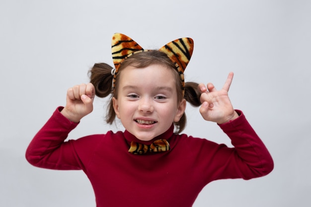 Photo a little girl in a burgundy turtleneck and with a rim with tiger ears on a white background with a place for text