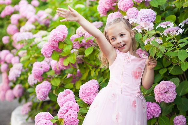 Little girl in bushes of hydrangea flowers.