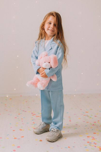 Photo little girl in a business blue pantsuit with a toy rabbit in her hands stands on a gray background