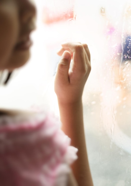 Little girl by window with raindrops on it on a rainy day