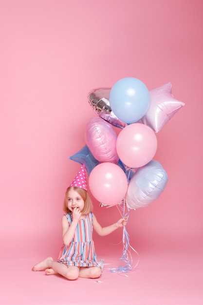 Little girl in a cap sits with a bunch of balloons